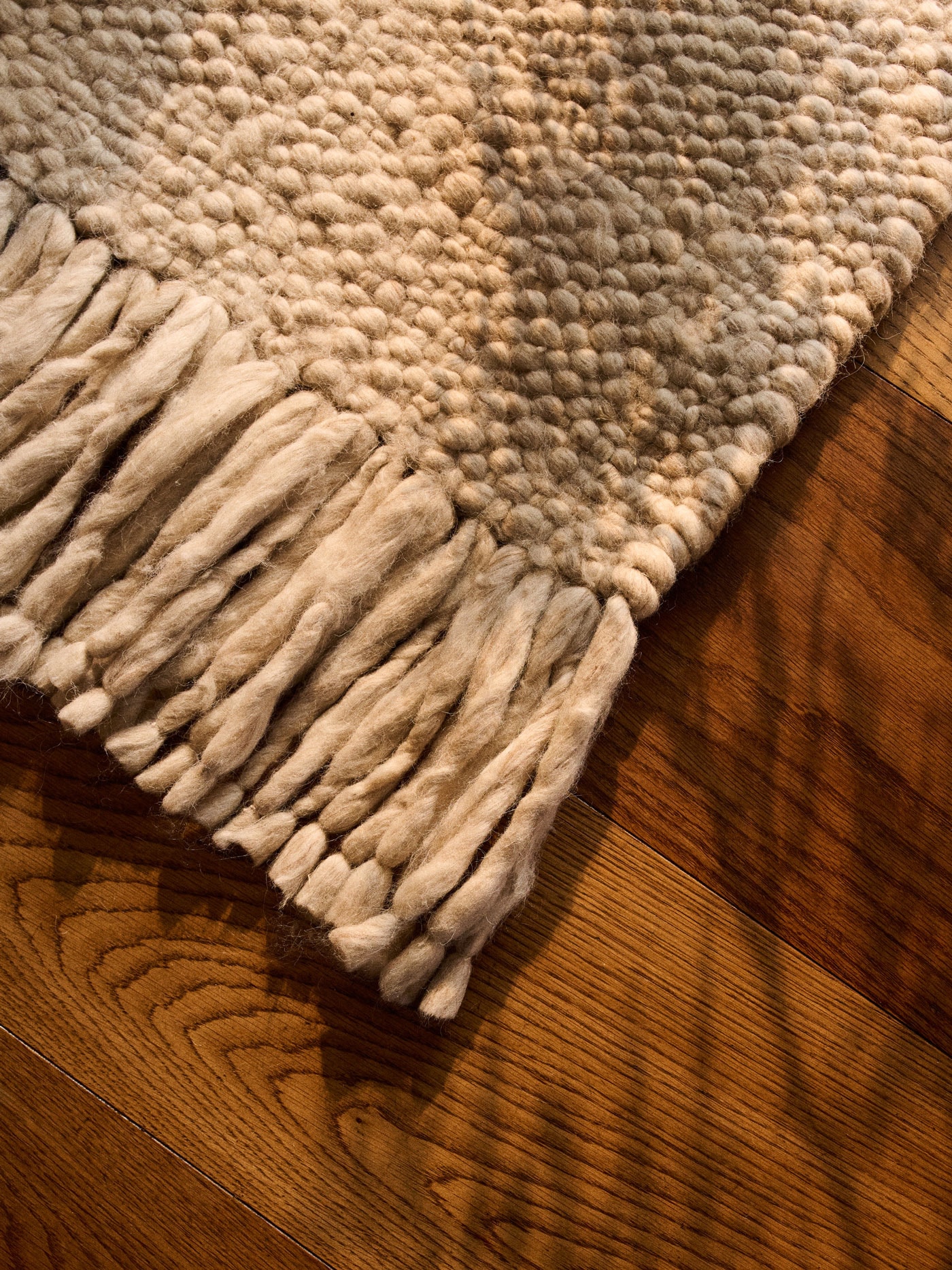 white wool rug with fringes on a dark wooden floor